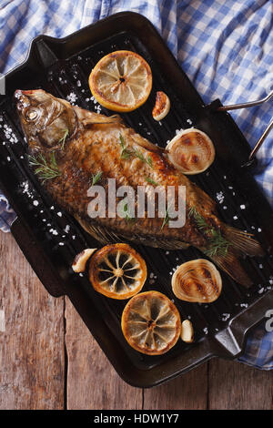 La carpe grillée avec du citron dans une poêle grill, vertical Vue de dessus close-up, style rustique Banque D'Images