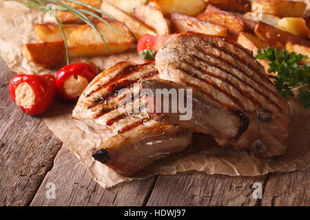Steak de porc grillé avec des pommes de terre et légumes close up sur papier, style rustique horizontale. Banque D'Images
