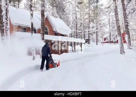 Homme avec une souffleuse à neige effacement d'une entrée de cour en face de la maison après une tempête de neige dans la région de Muskoka, Ontario, Canada Banque D'Images