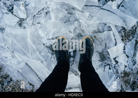 Les jambes dans des bottes de cuir homme debout sur la glace fissurée, vue du dessus Banque D'Images