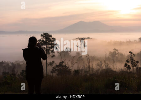 Les femmes asiatiques silhouette photographie prendre une photo avec beau lever de soleil dans le brouillard de l'environnement en forêt à Thung Salaeng Luang Parc National Pr Phetchabun Banque D'Images
