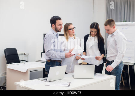 Groupe de quatre différents les hommes et les femmes dans des vêtements décontractés talking in office Banque D'Images