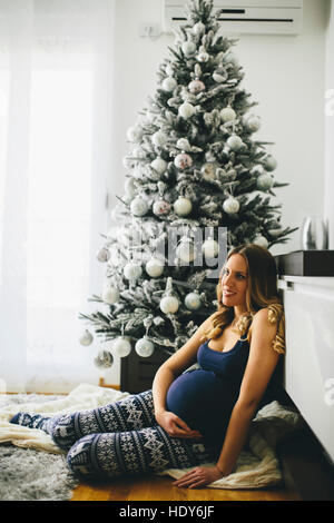 Femme enceinte à la maison près de l'arbre de Noël Banque D'Images