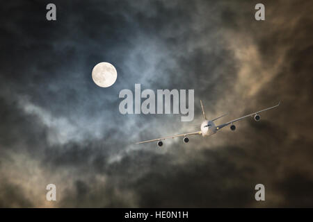 Avion de ligne de passagers non-stop fait vol de nuit à la lumière de la pleine lune à travers les nuages de tempête dans des conditions de turbulence Banque D'Images