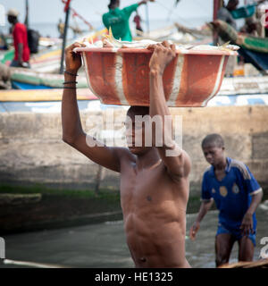 Jeune homme africain exerçant son grand bol de poisson de navire au rivage Banque D'Images