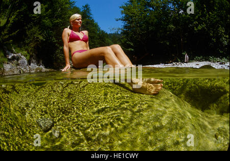 21-year-old femme assise sur un rocher dans un ruisseau de montagne, reposant ses pieds dans l'eau, Reichraming, Haute Autriche, Autriche Banque D'Images