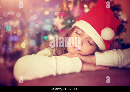 Portrait d'une belle teen girl wearing Santa hat sleeping rouge près de l'arbre de Noël en prévision d'un des cadeaux et le Père Noël, veille de Noël Banque D'Images