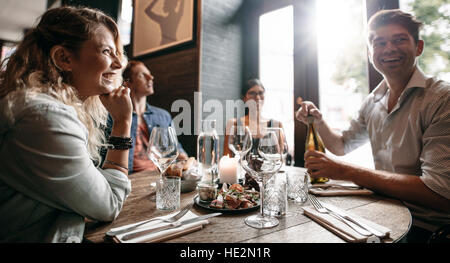 Groupe d'amis appréciant un repas du soir avec vin dans un restaurant. Heureux jeune homme et femme en train de dîner dans un restaurant. Banque D'Images