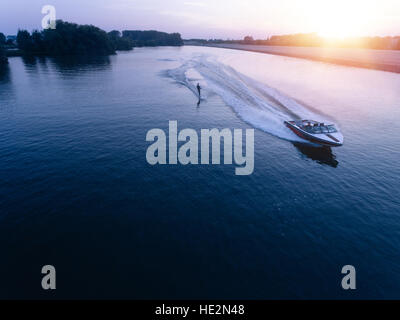 Vue aérienne de l'homme le wakeboard sur le lac au coucher du soleil. Le ski nautique sur le lac derrière un bateau. Banque D'Images