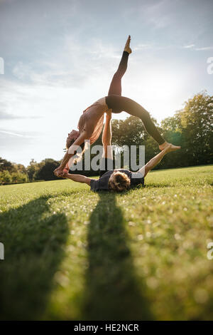 Shot verticale de sain jeune couple doing yoga acrobatique sur l'herbe. L'homme et la femme exerçant en paire au parc. Banque D'Images