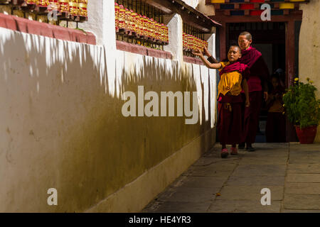 Deux moines bouddhistes s'en marchant le long du mur d'un bâtiment et filage gompa roues de prière Banque D'Images