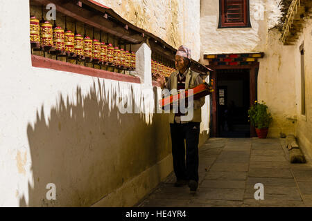 Un homme, tenant un livre de prières, est en marchant le long du mur d'un bâtiment et filage gompa roues de prière Banque D'Images