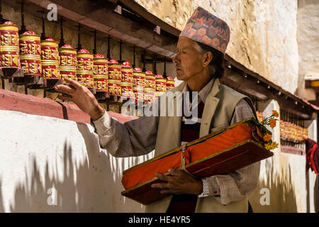 Un homme, tenant un livre de prières, est en marchant le long du mur d'un bâtiment et filage gompa roues de prière Banque D'Images