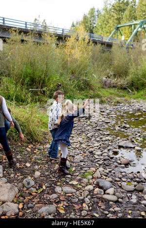 Frères et sœurs jeter des pierres dans la rivière McKenzie ensemble dans le style de photo de l'enfant s'amusant à jouer. Banque D'Images