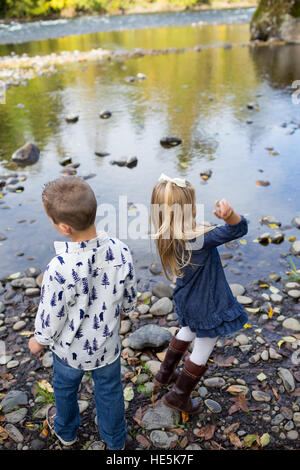 Frères et sœurs jeter des pierres dans la rivière McKenzie ensemble dans le style de photo de l'enfant s'amusant à jouer. Banque D'Images