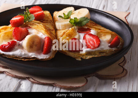 Crêpes maison avec des fraises, des bananes et de la crème sur une plaque horizontale. Banque D'Images