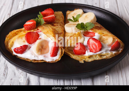 Deux crêpes avec fraises, bananes et de la crème sur une plaque horizontale. Banque D'Images