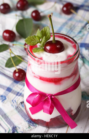 Crème fouettée avec une cerise dans un pot de verre close up vertical. Banque D'Images