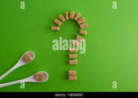 Brown Sugar cubes en forme de point d'interrogation sur fond de verdure. Vue d'en haut. Pour régimes unhealty sweet addiction concept Banque D'Images