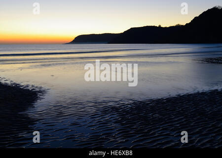 Coucher du soleil orange reflétée sur la plage à marée haute dans une baie abritée sur la péninsule de Gower- Caswell Bay Banque D'Images