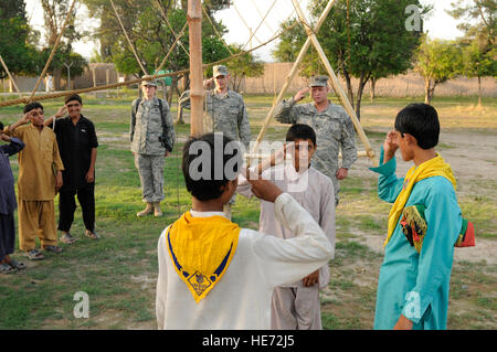 Boy Scouts afghans effectuer une descente du drapeau cérémonie au cours de leur réunion hebdomadaire, tandis que des troupes de l'ARMÉE AMÉRICAINE Le Capitaine Glenn Battschinger, Nangarhar, Équipe provinciale de reconstruction de l'Équipe des affaires civiles et la troupe scoute du Maître, U.S. Air Force 1er lieutenant Jason Baker, PRT'adjoint au médecin, et le capitaine de l'US Air Force Mary Danner-Jones, officier des affaires publiques de l'EPR de prendre part à la base d'opérations avancée Finley Shields, Jalalabad, Afghanistan, le 31 juillet 2010. Banque D'Images