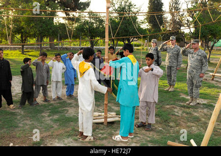 Boy Scouts afghans effectuer une descente du drapeau cérémonie au cours de leur réunion hebdomadaire, tandis que des troupes de l'ARMÉE AMÉRICAINE Le Capitaine Glenn Battschinger, Nangarhar, Équipe provinciale de reconstruction de l'Équipe des affaires civiles et la troupe scoute du Maître, U.S. Air Force 1er lieutenant Jason Baker, PRT, Assistant les médecins et le capitaine de l'US Air Force Mary Danner-Jones, officier des affaires publiques de l'EPR de prendre part à la base d'opérations avancée Finley Shields, Jalalabad, Afghanistan, le 31 juillet 2010. Banque D'Images