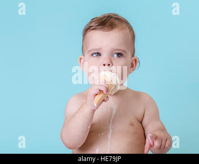 Joli bébé fille avec de la crème glacée fondue sur fond bleu clair Banque D'Images