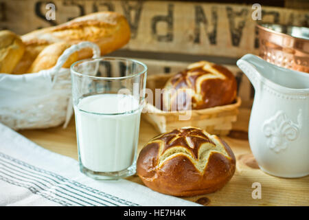 Lye frais bobines dans un panier en osier, un verre de lait, blanc cruche sur une table en bois dans un style rustique cuisine intérieur Banque D'Images