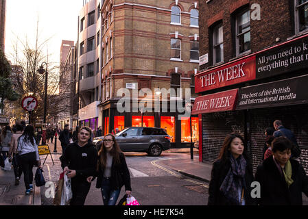 Les gens qui marchent dans la Broadwick Street, Soho, Londres en face d'une fermeture de boutique avec de grands magazines signe sur l'avant la promotion de la revue britannique la semaine Banque D'Images