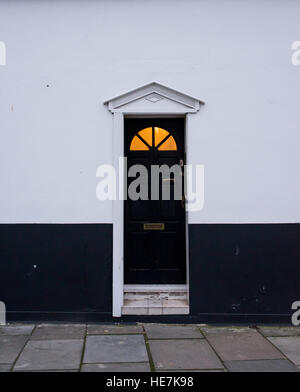 Victorien en bois noir porte sur un mur noir et blanc avec panneau en verre sur le dessus et jaune chaud lumière provenant de l'intérieur Banque D'Images