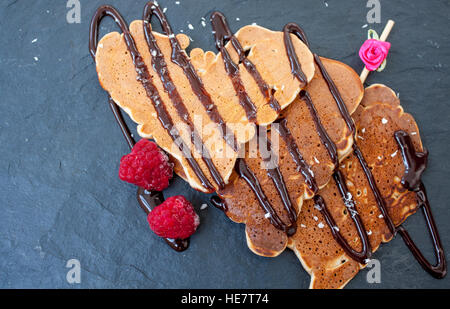 Des crêpes en forme de coeur avec le sirop de chocolat et de framboises sur la Saint-Valentin. Banque D'Images