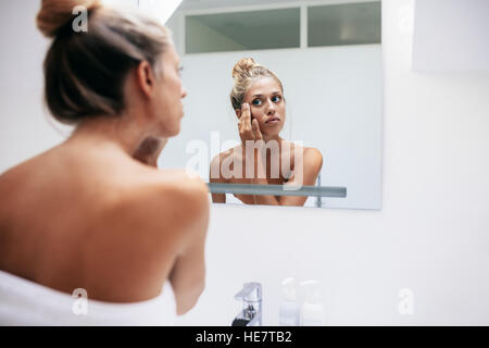 Beau young caucasian woman applying cream sur le visage dans la salle de bains à la maison. Femme prendre soin de visage peau. Banque D'Images