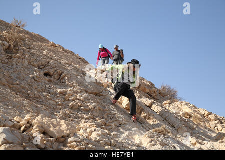 Une femme de randonneur âgée descend soigneusement une pente rocheuse très raide du Mont Massor en utilisant un bâton de randonnée pour éviter de tomber, désert de Negev. Banque D'Images