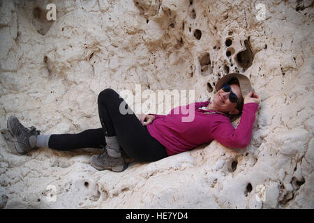 A 52 ans, femme, et sourit alors qu'elle se repose pendant une randonnée sur une étagère dans la paroi rocheuse d'un canyon dans le désert du Néguev. Banque D'Images