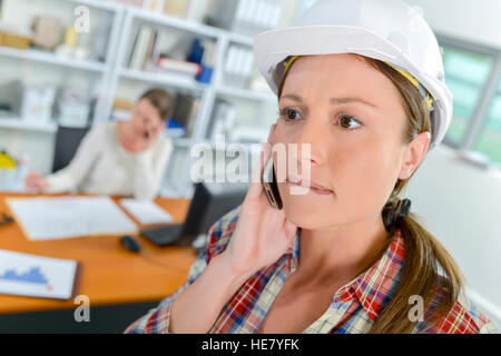 Lady wearing hardhat, on cellphone biting lip Banque D'Images