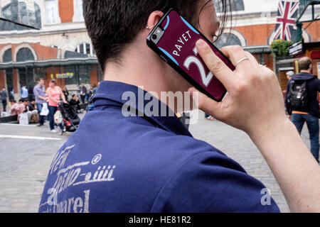 Un jeune fan de West Ham United fait un appel de son téléphone intelligent. Le téléphone est doté d'un couvercle de protection portant le nom Payet et 27 Banque D'Images