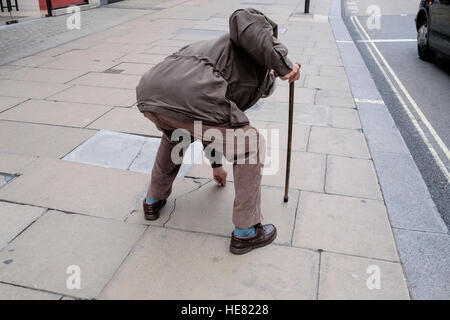 Homme âgé utilise une canne pour soutenir comme il se penche pour ramasser un élément de la chaussée Banque D'Images