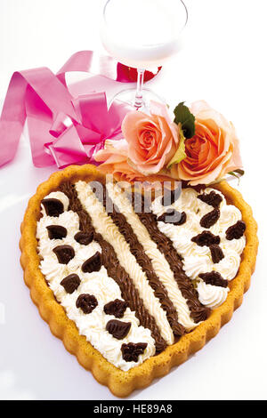 Tarte à la crème en forme de cœur orné de roses en face d'un verre de champagne et un ruban Banque D'Images