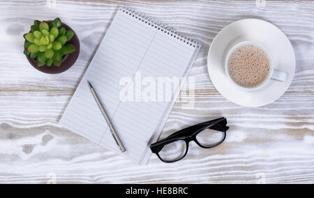 Carnet et un stylo avec des lunettes de lecture, et des plantes de café crémeux sur tableau blanc rustique Banque D'Images