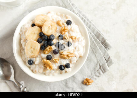 Bouillie d'avoine avec des noix, des bleuets et de la banane dans un bol - petit-déjeuner rustique de sain Banque D'Images