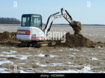 Un Bobcat 331E mini-pelle creuse une partie d'une ligne d'eau près de l'extrémité approche de la piste 32 lors d'un projet de travaux publics entrepris par le 436e Escadron de génie civil, les garçons 'taxi truck', le 21 mars 2014, à Dover Air Force Base, Del. Poches de neige peut être vu dans le domaine au cours de cette fouille par temps froid. Greg L. Davis) Banque D'Images
