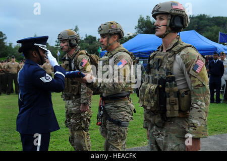 Le chef de l'US Air Force Master Sgt. Colon-Lopez Ramon, chef du commandement de l'escadre 18, présente le drapeau américain à un membre de la garde d'honneur de Kadena avec l'aide du personnel Le Sgt. George Reed (à gauche) et le sergent. La Jordanie Sainte-claire (à droite), à la fois pararescuemen du 31ème escadron de sauvetage, au cours d'une cérémonie à la Journée des anciens combattants de Kadena Air Base, Japon, le 11 novembre, 2013. Dans le cadre de la Journée des anciens combattants cérémonie, pararescuemen descendu en rappel depuis un hélicoptère HH-60 Pave Hawk avec le drapeau américain. Le s.. L'Amber E. N. Jacobs) Banque D'Images