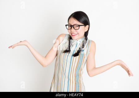 Portrait de jeune fille asiatique en robe qipao traditionnelle incertain et haussant les épaules, debout sur fond uni. Banque D'Images