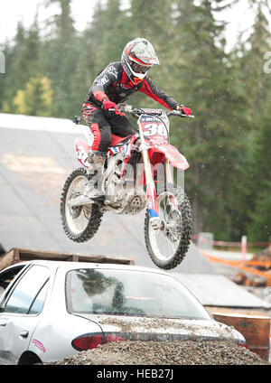 Un pilote d'enduro motorcross chevauche son vélo sur une voiture accidentée au Parc olympique de Whistler. Whistler, BC, Canada Banque D'Images