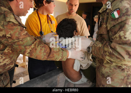 Le Major Italien Damiano Morici, infirmier, et le lieutenant Fabrizio Dell'Aglio, tous deux de l'Italien du Sud Groupe de travail, tenir un jeune Afghan qui a été victime d'un attentat-suicide à Farah ville autour de 9 heures, le 20 novembre, afin de frégate américaine. Nancy Delaney, un médecin affecté à la base d'opération avancée Farah, peut inspecter le dos du garçon pour les blessures. Le kamikaze conduisant une moto s'est fait exploser tuant 16 personnes et blessant 34 autres. L'attaque a eu lieu près de la province de Farah et gouverneur du après Farah est devenu l'hôpital submergé de blessés, 22 hommes Afghans blessés ont été transportés à Fara FOB Banque D'Images