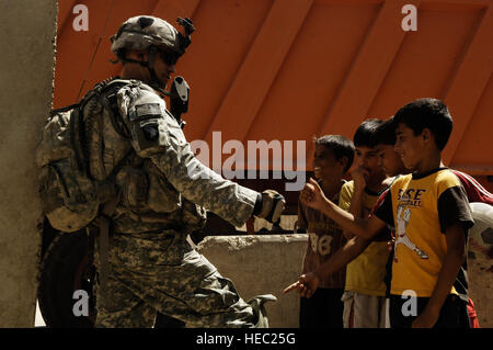 Le sergent de l'armée américaine. Jeremiah Johnson, natif de Gastonia, N.C., joue avec les garçons irakiens debout à côté de lui alors qu'arrêtée au cours d'une patrouille dans la région de Shula, l'Iraq le 19 juillet 2008. Les soldats américains font partie du 2e peloton, Compagnie Bravo, 1er bataillon du 502e Régiment d'infanterie, 101ème Division aéroportée. Banque D'Images
