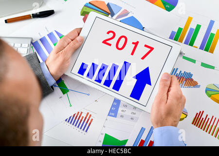 Libre d'un jeune homme de race blanche à son bureau bureau plein de graphiques et tableaux l'observation d'une prévision de croissance économique pour l'année 2017 dans son Banque D'Images