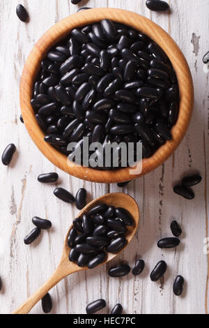 Les haricots noirs dans une cuillère en bois et un bol fermer vers le haut sur la table. vertical vue d'en haut Banque D'Images