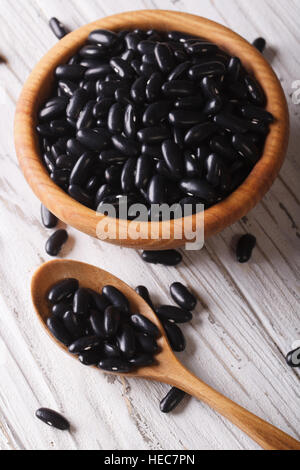 Les haricots noirs dans une cuillère en bois et un bol sur une table close-up vertical, style rustique. Banque D'Images