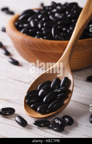 Les haricots noirs dans une cuillère en bois et un bol sur une table close-up. Rustique, vertical Banque D'Images